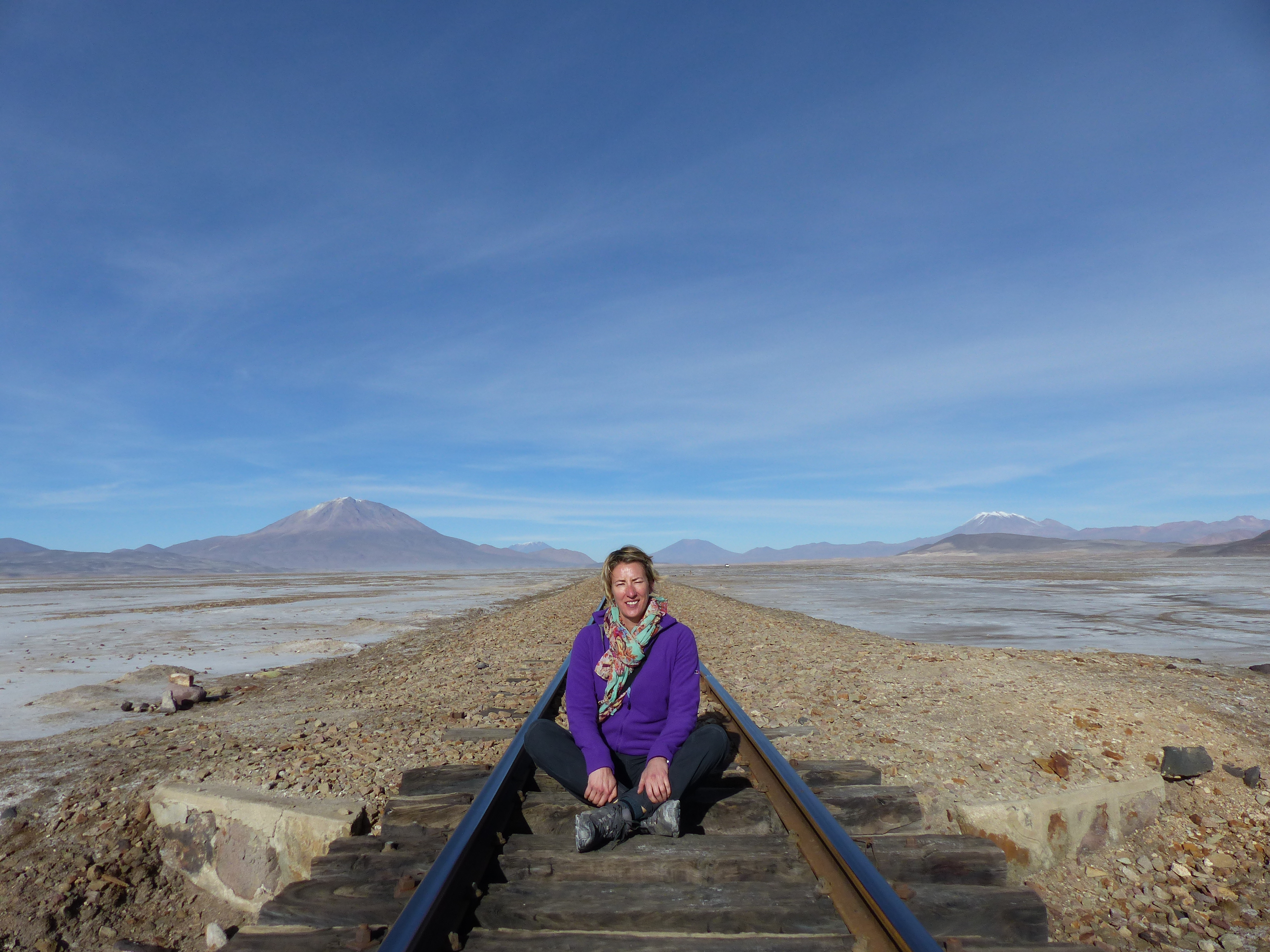 Woman sitting on train tracks which disappear into the distance behind her