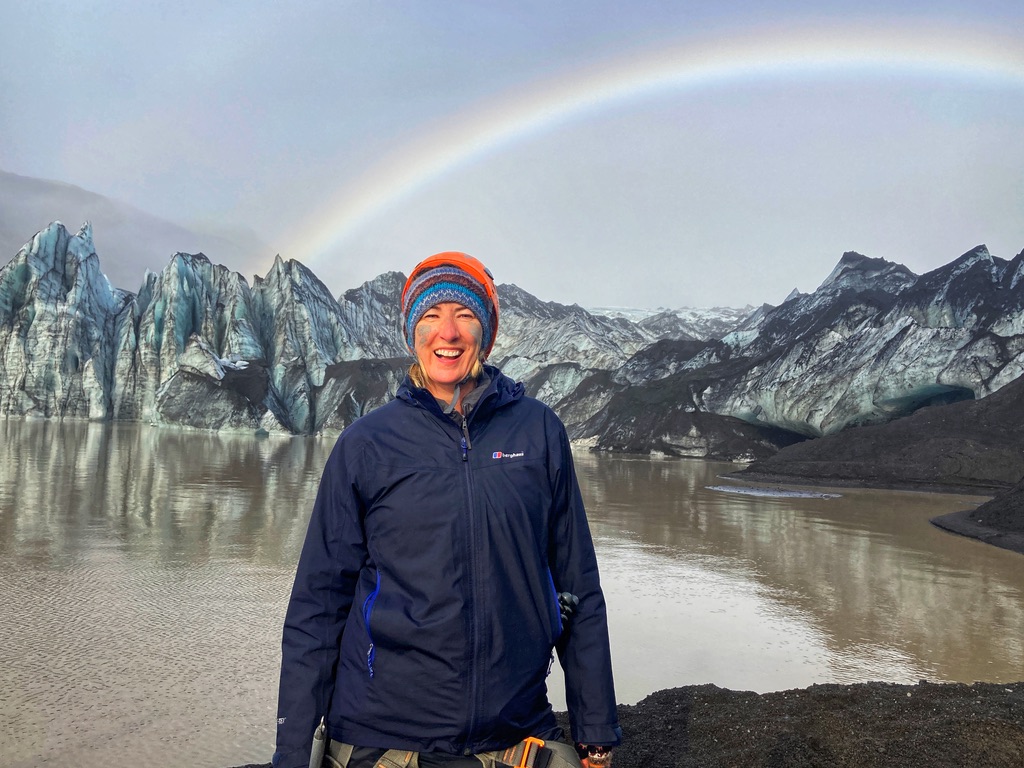 Woman standing in front of a glacier with a rainbow over the top